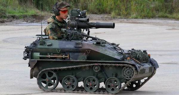 A soldier operating a tracked, armored reconnaissance vehicle equipped with a mounted heavy machine gun.