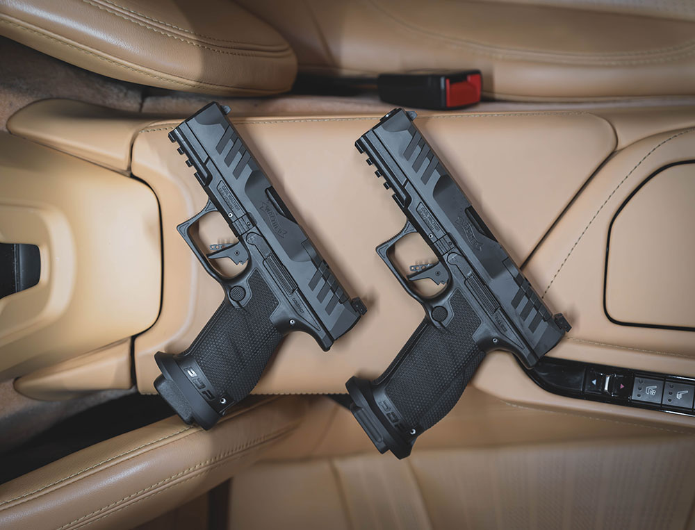 Two black pistols are placed on tan leather seats inside a vehicle, positioned side by side near the car's center console.