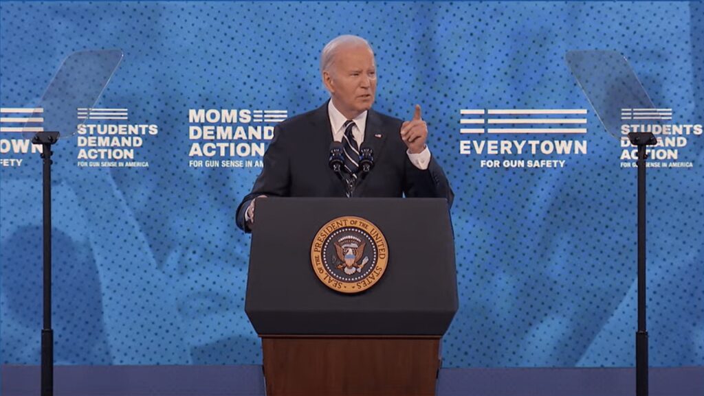 A man standing at a podium with a seal of the President of the United States, speaking at an event with text in the background: "Moms Demand Action," "Students Demand Action," and "Everytown for Our Safety.