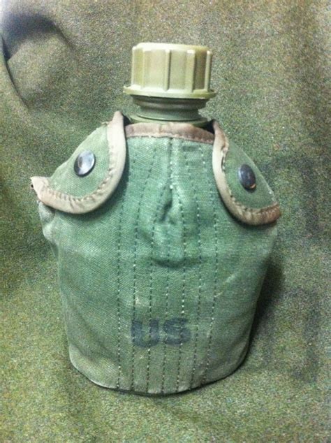 A military-style green water canteen with the letters "US" printed on the cover, featuring a secured cap and buttoned flap closure.
