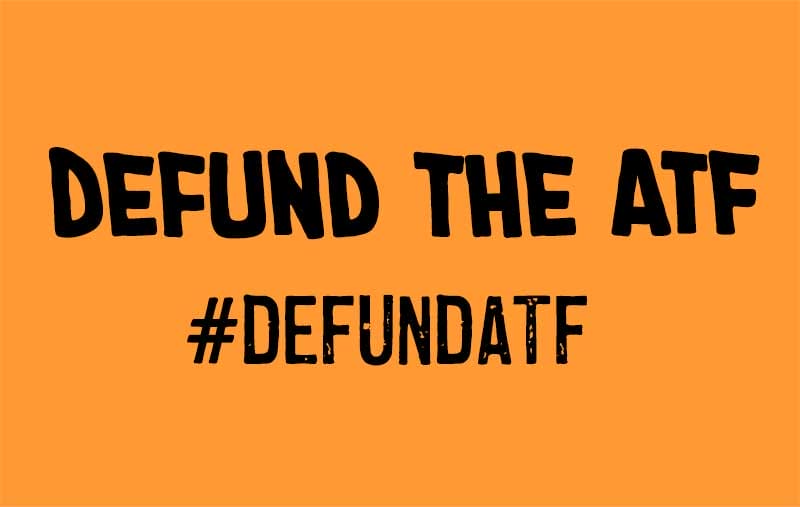 An orange sign with the text "DEFUND THE ATF" and the hashtag "#DEFUNDATF" in black, bold letters.