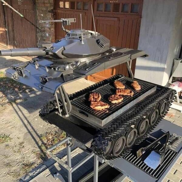 A tank-shaped grill with grilled meat on the grilling surface, situated outdoors near a building with brown doors.