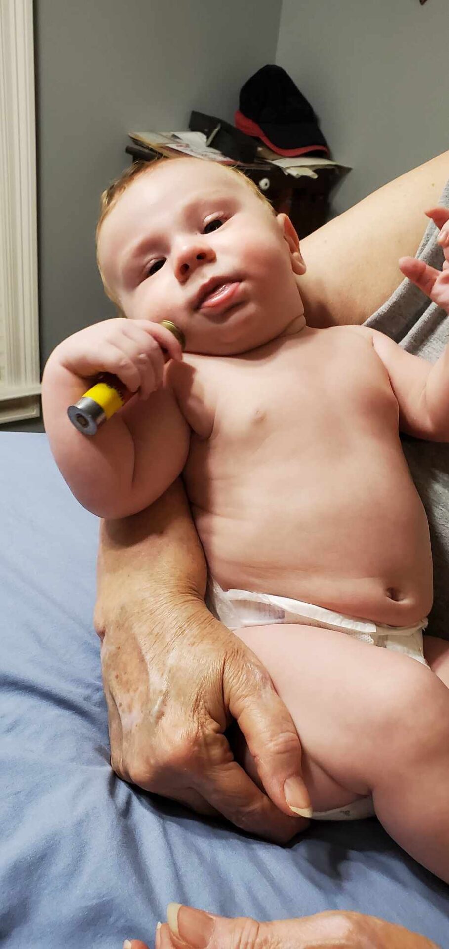 A baby wearing a diaper is held by an adult and holding a small object in its hand.