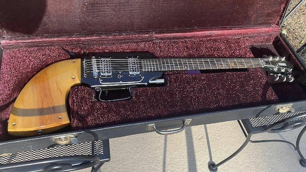 A unique guitar gun with a wooden body and distinctive design is displayed in an open, velvet-lined hard case.