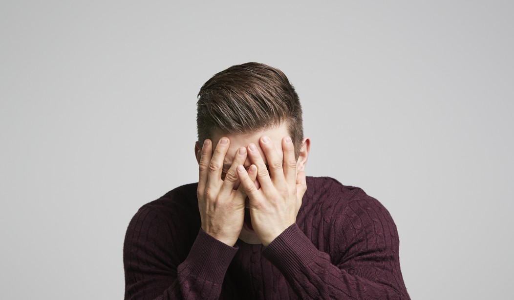 A person in a maroon sweater covers their face with both hands against a plain background.