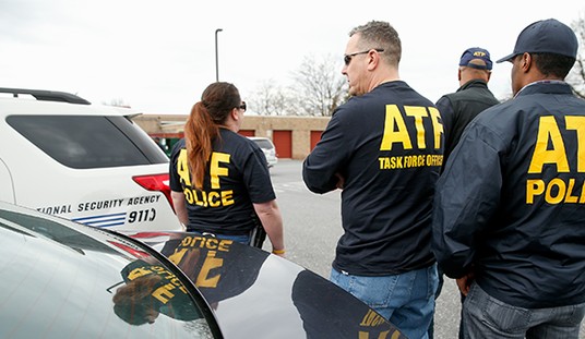 Three people wearing ATF police jackets stand near law enforcement vehicles in a parking lot.