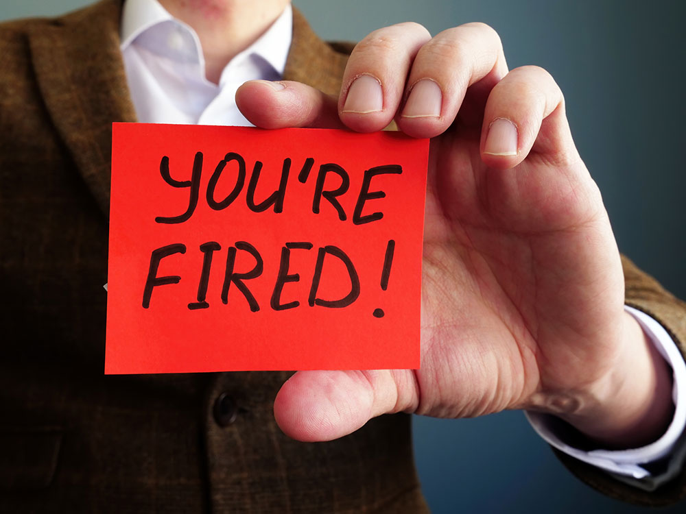 Person holding a red card with the text "You're Fired!" written in bold black letters.