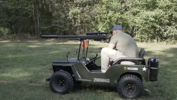 A man sits on a small green utility vehicle in a grassy area, aiming a long-barreled firearm mounted on the front. Trees are visible in the background.