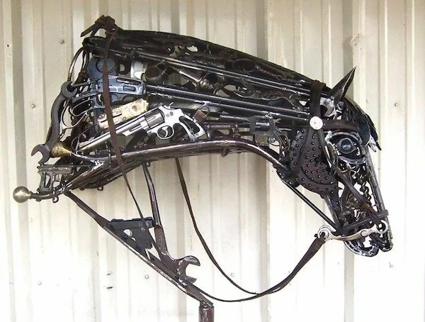 A metal horse head sculpture made from various tools, gears, and mechanical parts, mounted against a corrugated metal wall.