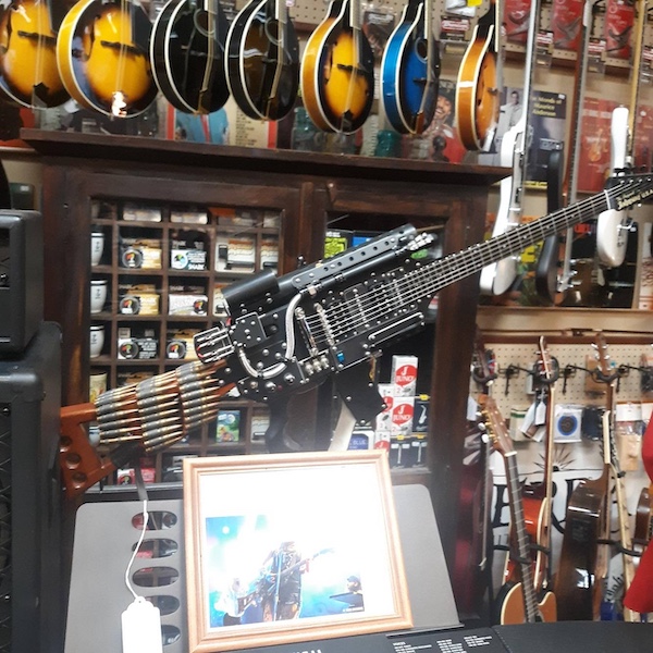 Electric guitar modified to resemble a machine gun, displayed in a music store among other instruments and accessories.