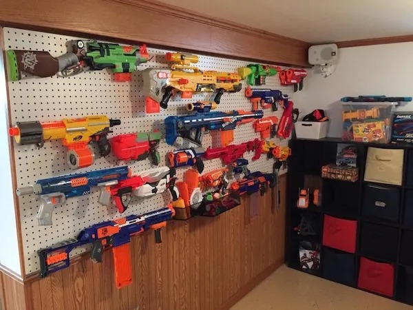 A pegboard wall displays a large collection of toy Nerf blasters; nearby shelves hold more Nerf toys, bins, and boxes.