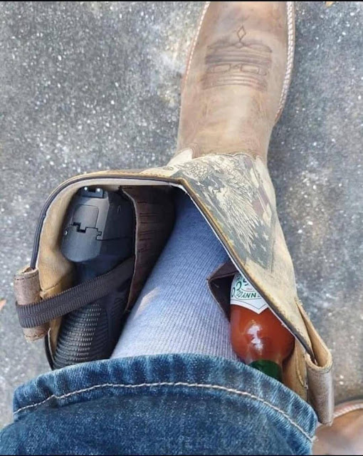 A person wearing a cowboy boot holds a handgun and a small bottle of hot sauce inside the boot, with jeans and a grey sock visible.