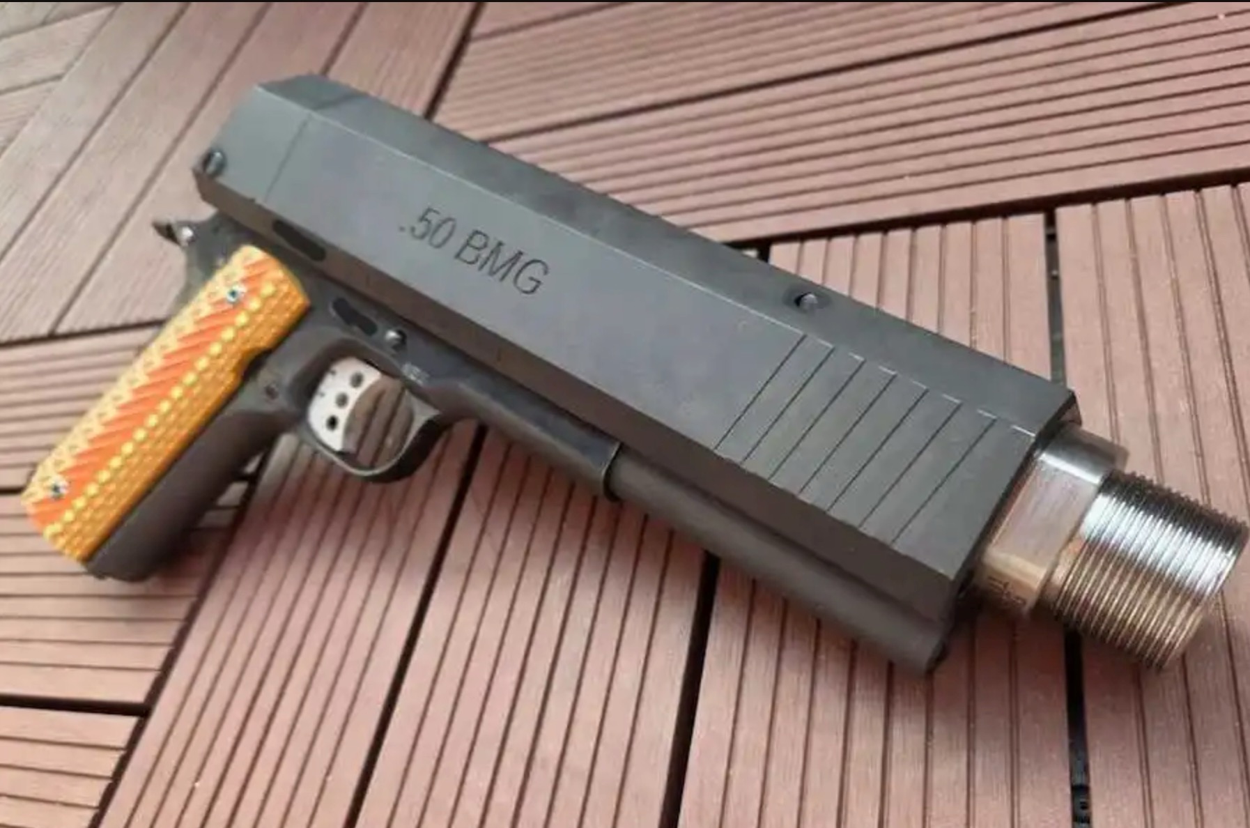 A large pistol with a wooden grip and a matte black slide engraved ".50 BMG," featuring an oversized threaded barrel, resting on a wooden surface.