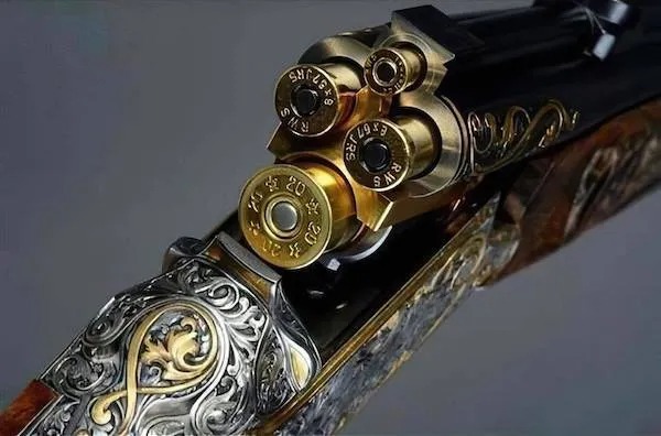 Close-up of an intricately engraved shotgun with its chamber open, showing loaded and spent shotgun shells.