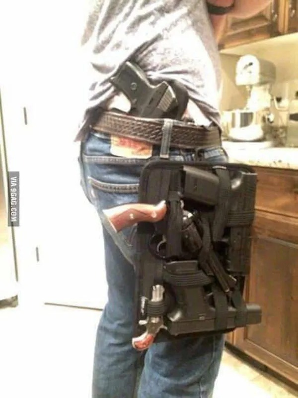 A person wearing jeans and a belt holster carrying multiple handguns is standing in a kitchen.