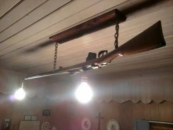 A rifle mounted upside down on the ceiling, serving as a light fixture with two hanging light bulbs.