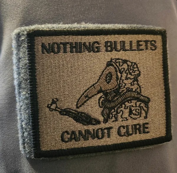 A fabric patch features an image of a plague doctor and the words "NOTHING BULLETS CANNOT CURE" embroidered in capital letters.