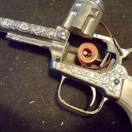 Close-up of a decorative toy revolver labeled "Pony Boy," showing a rolled-up cap gun strip loaded in the chamber.