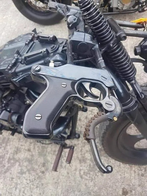 Close-up of a motorcycle handle shaped like a black handgun, with the trigger serving as the brake lever.