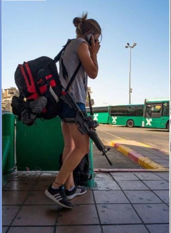A woman wearing casual clothes and a large backpack walks while talking on a phone and carrying a rifle at a bus station with green buses in the background.